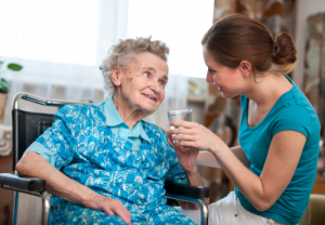 caregiver giving medication to an elderly woman in wheelchairs