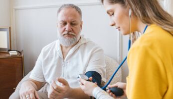 A healthcare professional checks an elderly man's blood pressure in a cozy room.